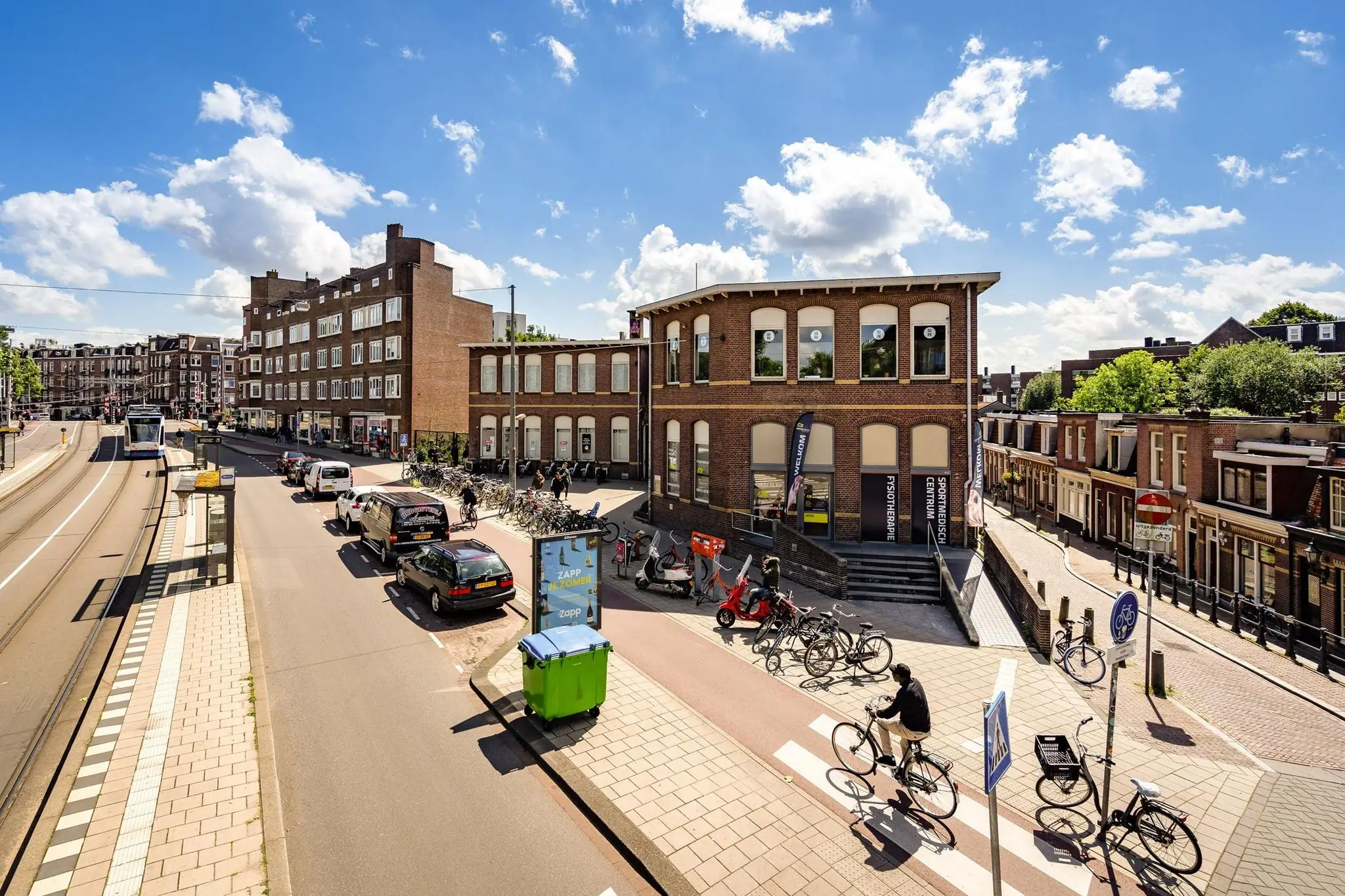 Straatbeeld van de Admiraal de Ruijterweg in Amsterdam met fietsers, auto’s, een tram en een karakteristiek bakstenen gebouw.